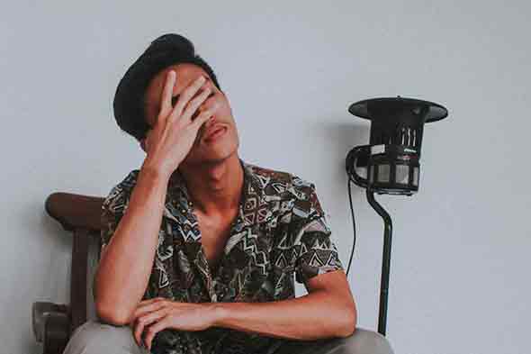 A man sitting on a wooden chair with his hand on his face.