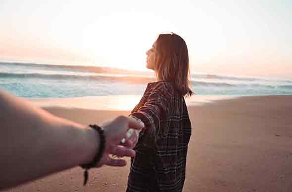 woman holding hand while facing the ocean