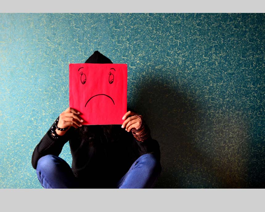 girl holding up a sad smiley hiding her face